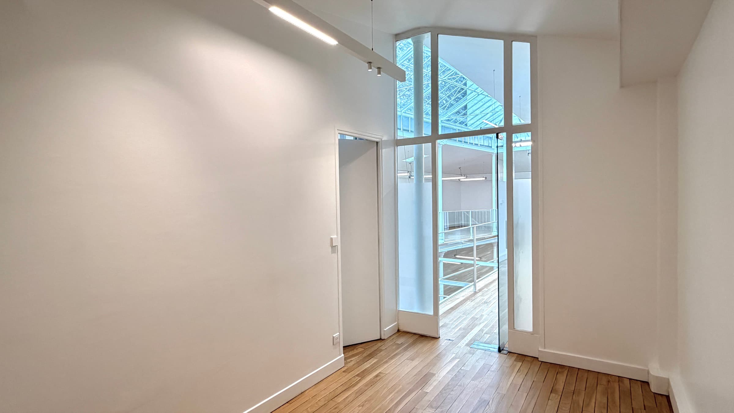 Palier des bureaux au 1er étage en parquet avec baie vitrée donnant sur la mezzanine et la verrière