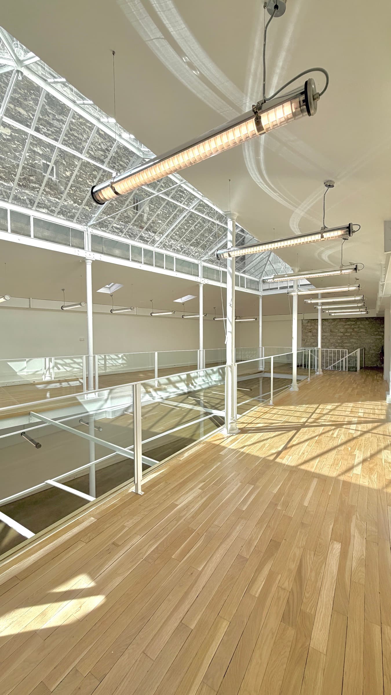 Coursive de la mezzanine baignée de soleil avec suspensions industrielles et mur en pierre