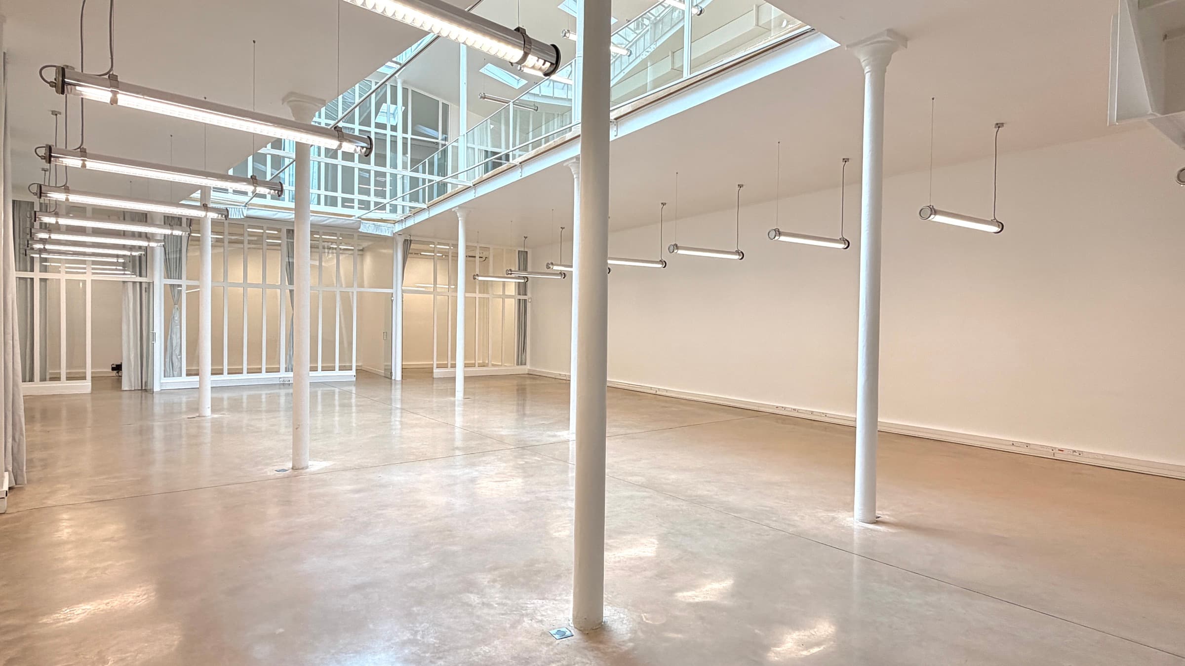 Plateau RDC double hauteur avec cloisons verrières blanches et luminaires allumés