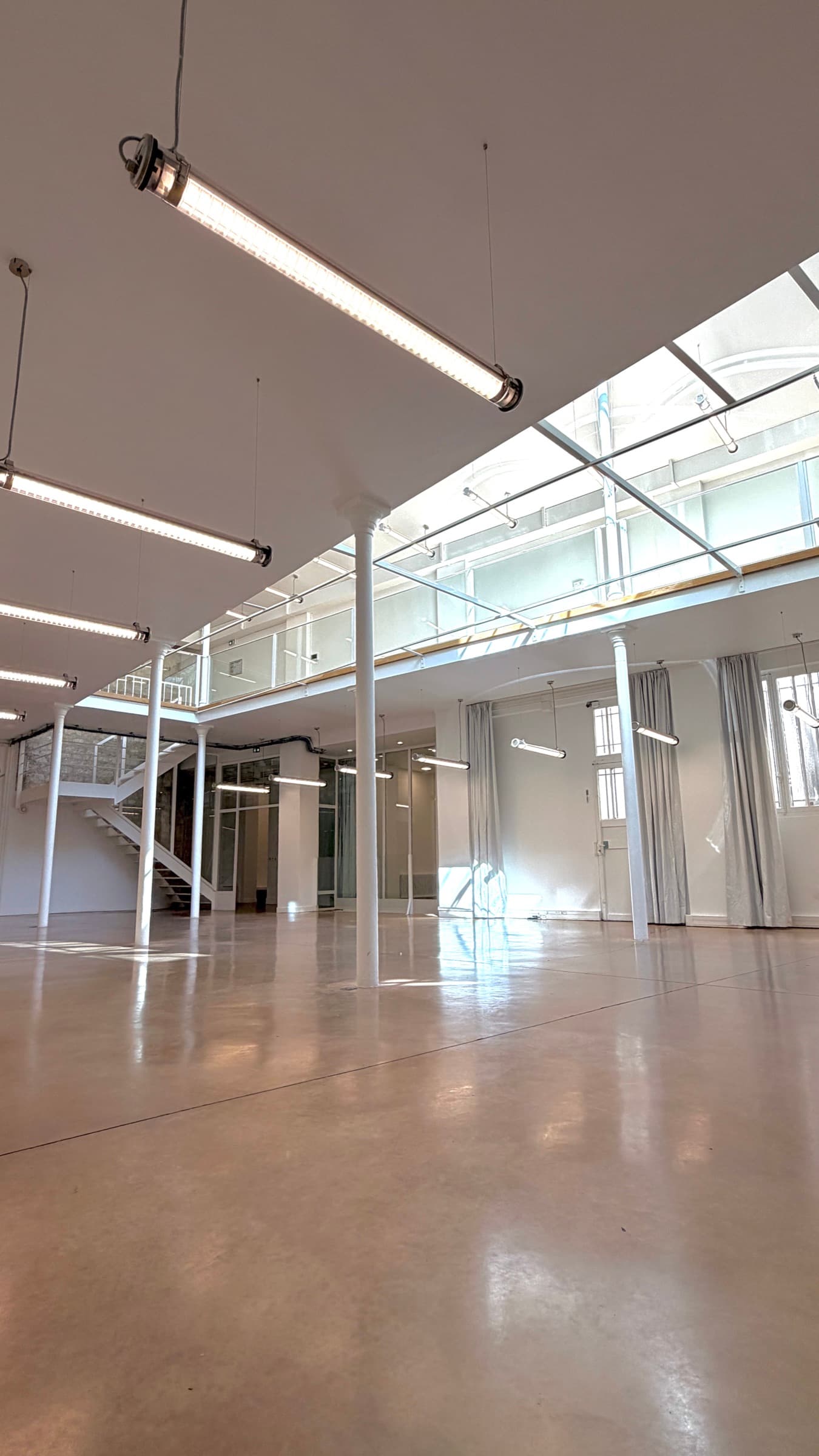 Plateau RDC vu sous la mezzanine avec colonnes blanches et escalier blanc contre le mur en pierre