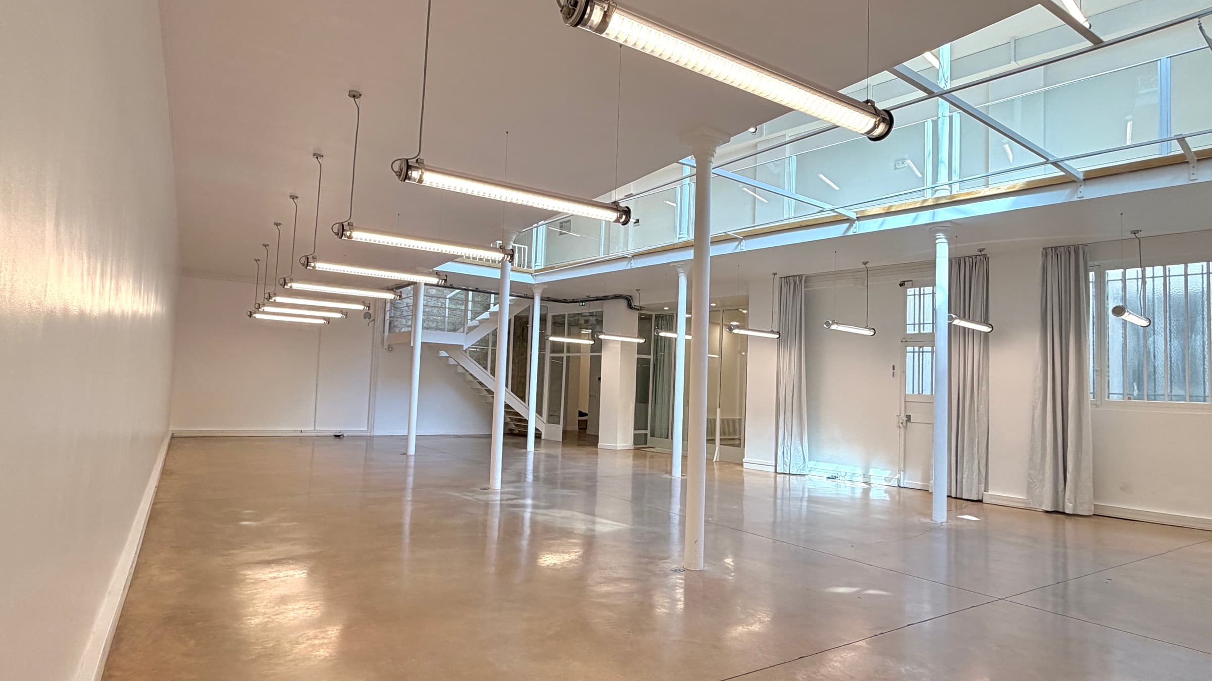 Plateau du RDC avec alignement de néons suspendus et escalier blanc au fond — location salle Paris