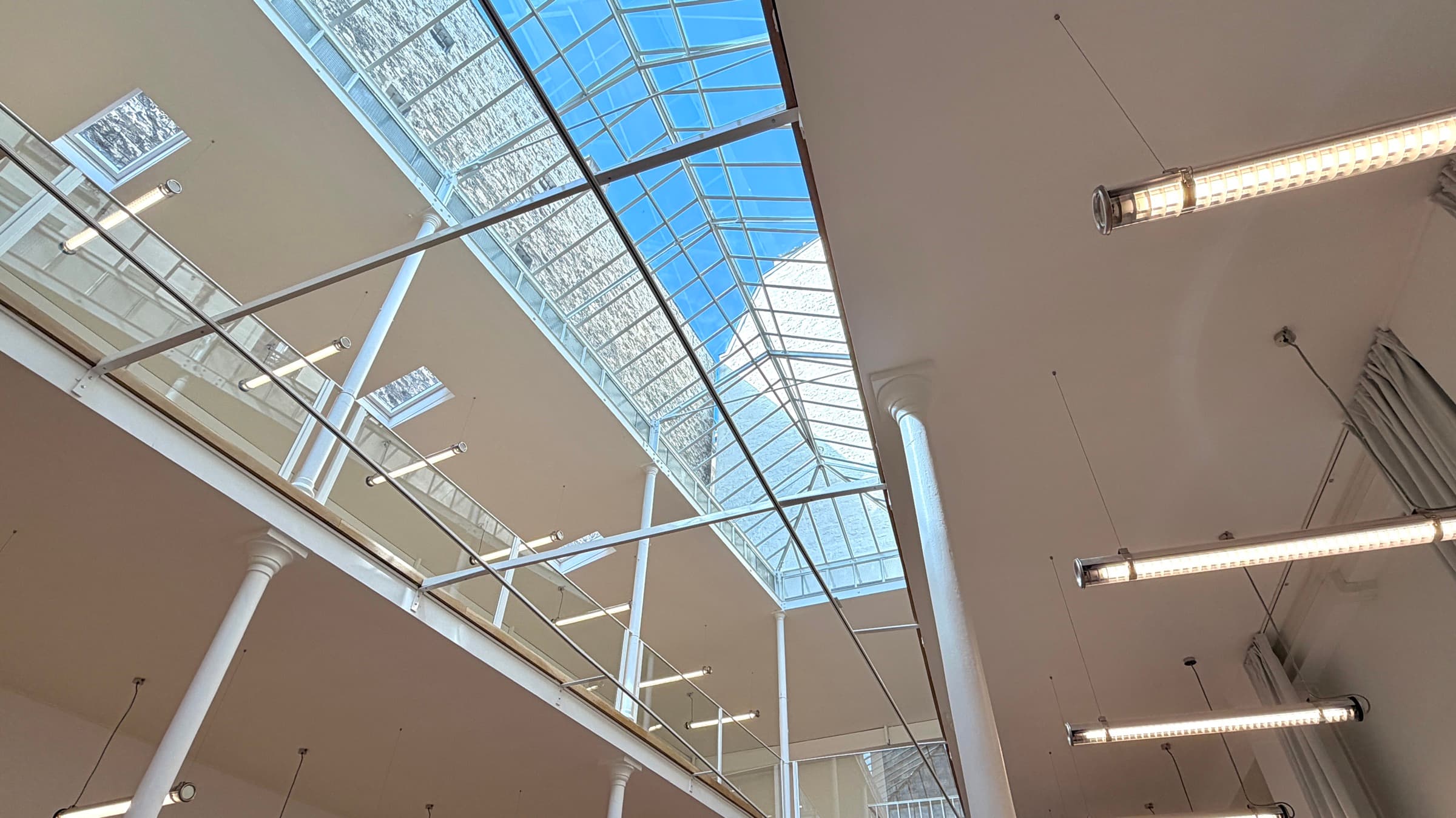 Contre-plongée sur la verrière zénithale, garde-corps de la mezzanine et néons suspendus