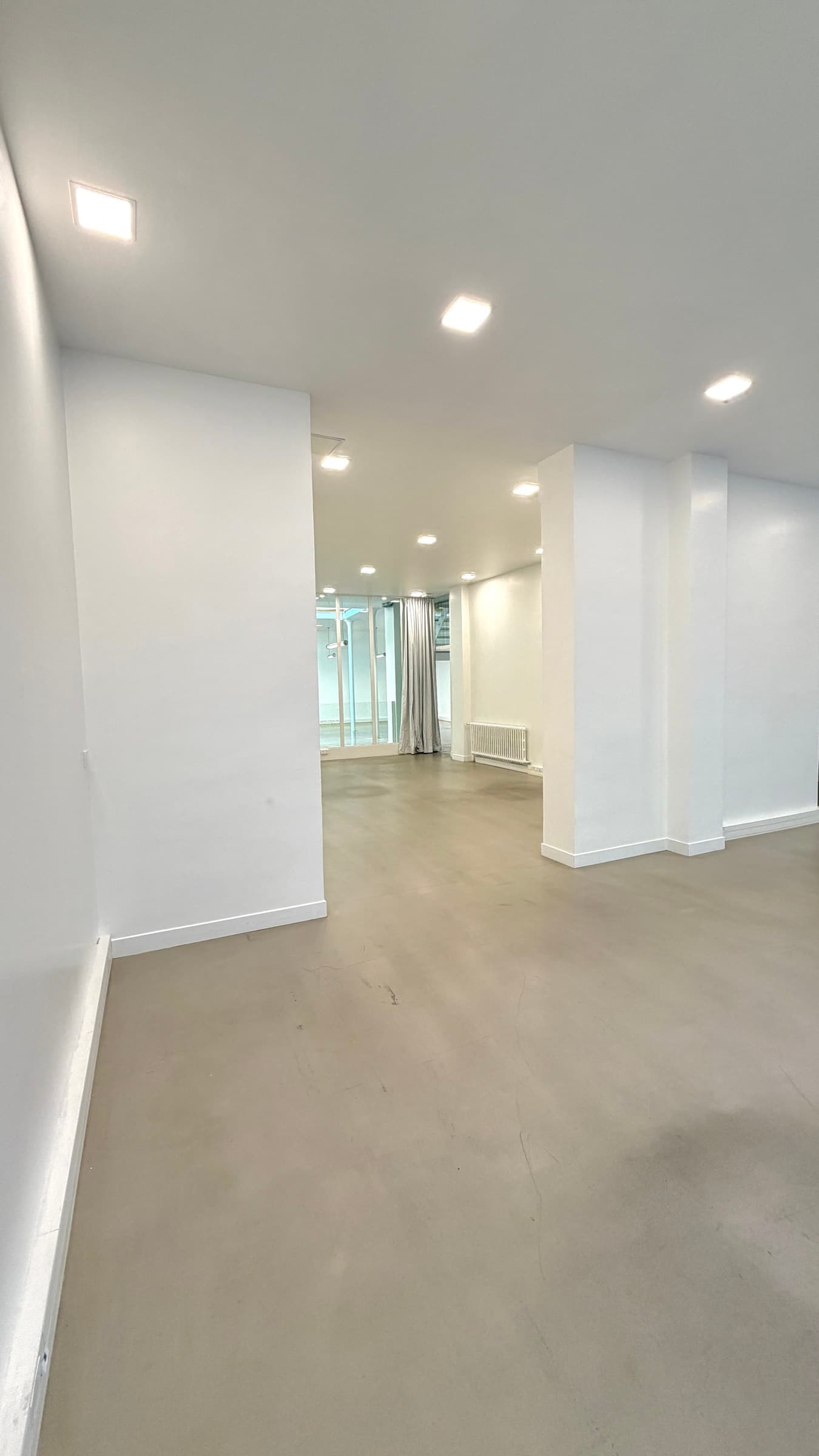 Salle blanche au sol béton ciré avec spots encastrés et baie vitrée à rideau